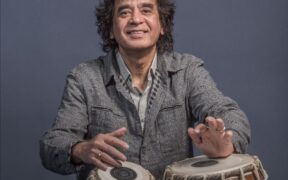 Tabla legend Zakir Hussain in a grey jacket playing tabla