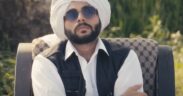 Akash Andaaz wearing white turban and white shirt with black vest and black sunglasses, sitting with arms crossed