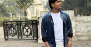 Ankit Tiwari wearing blue jacket over white t-shirt and trousers, looking up with a white dome structure in the background