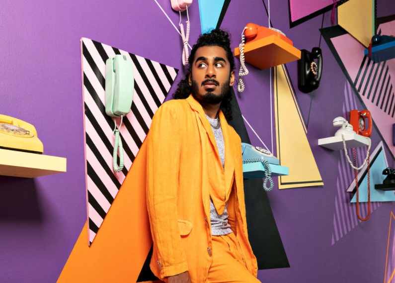 Pop artist Hrishi wearing orange suit standing in front of purple wall