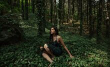 Singer-songwriter Swati Bhatt wearing green and seated in a forest surrounded by trees in daylight