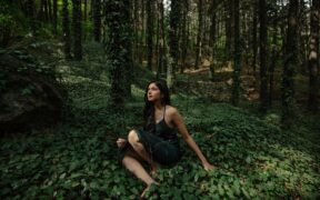 Singer-songwriter Swati Bhatt wearing green and seated in a forest surrounded by trees in daylight