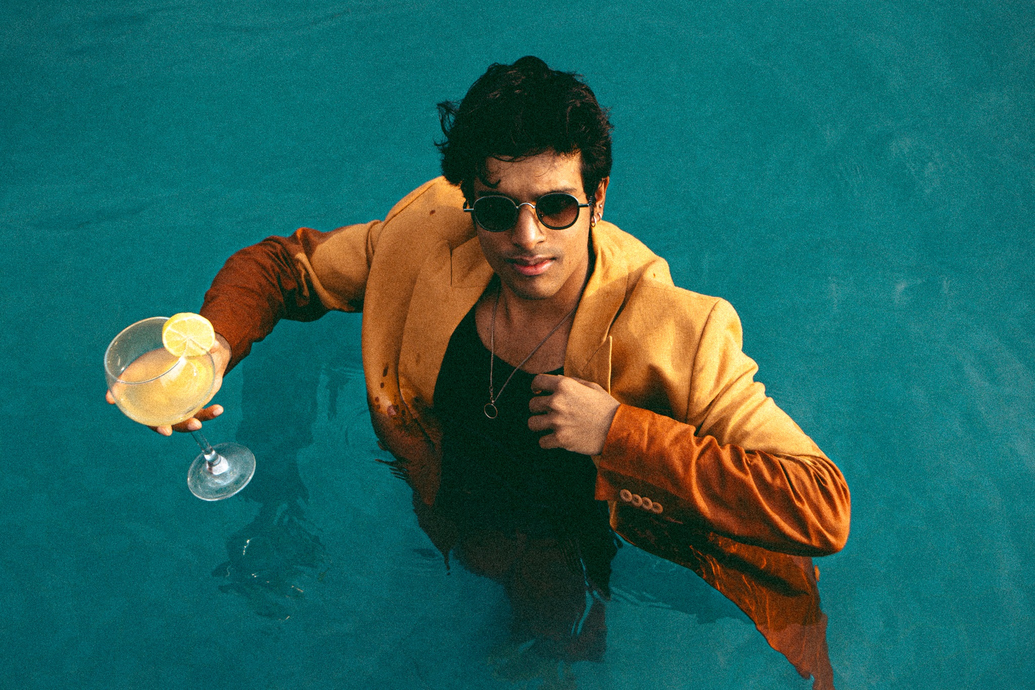 Singer Tarang Joseph in a pool wearing a suit with sunglasses and glass in hand