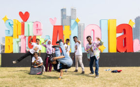 Hip-hop artists from Dharavi posing in front of a sign reading Shine Bright at Lolla