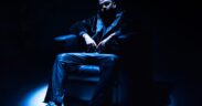 Rapper DRV aka Dhruv Rajpal wearing black seated on a couch under a spotlight