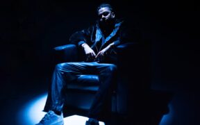 Rapper DRV aka Dhruv Rajpal wearing black seated on a couch under a spotlight