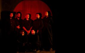 Members of The Down Troddence band with vocalist TM Krishna all wearing black and posing in red light