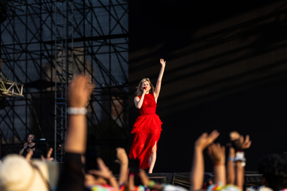 Aurora performing on stage in red dress, raising her hand to a crowd