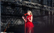 Aurora performing on stage in red dress, raising her hand to a crowd