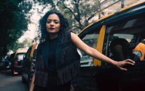 Singer Suman Sridhar weearing black dress and standing next to a taxi