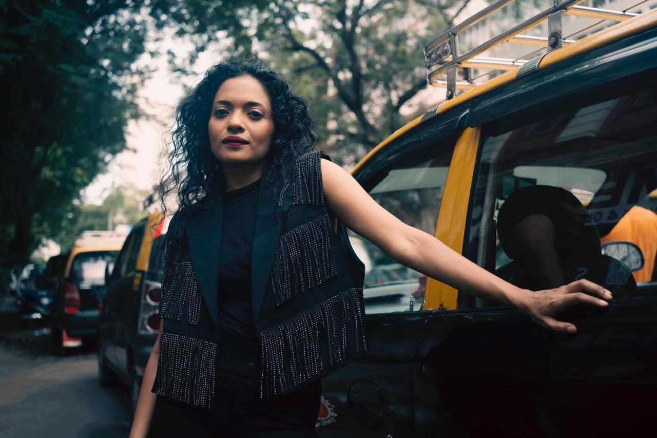 Singer Suman Sridhar weearing black dress and standing next to a taxi