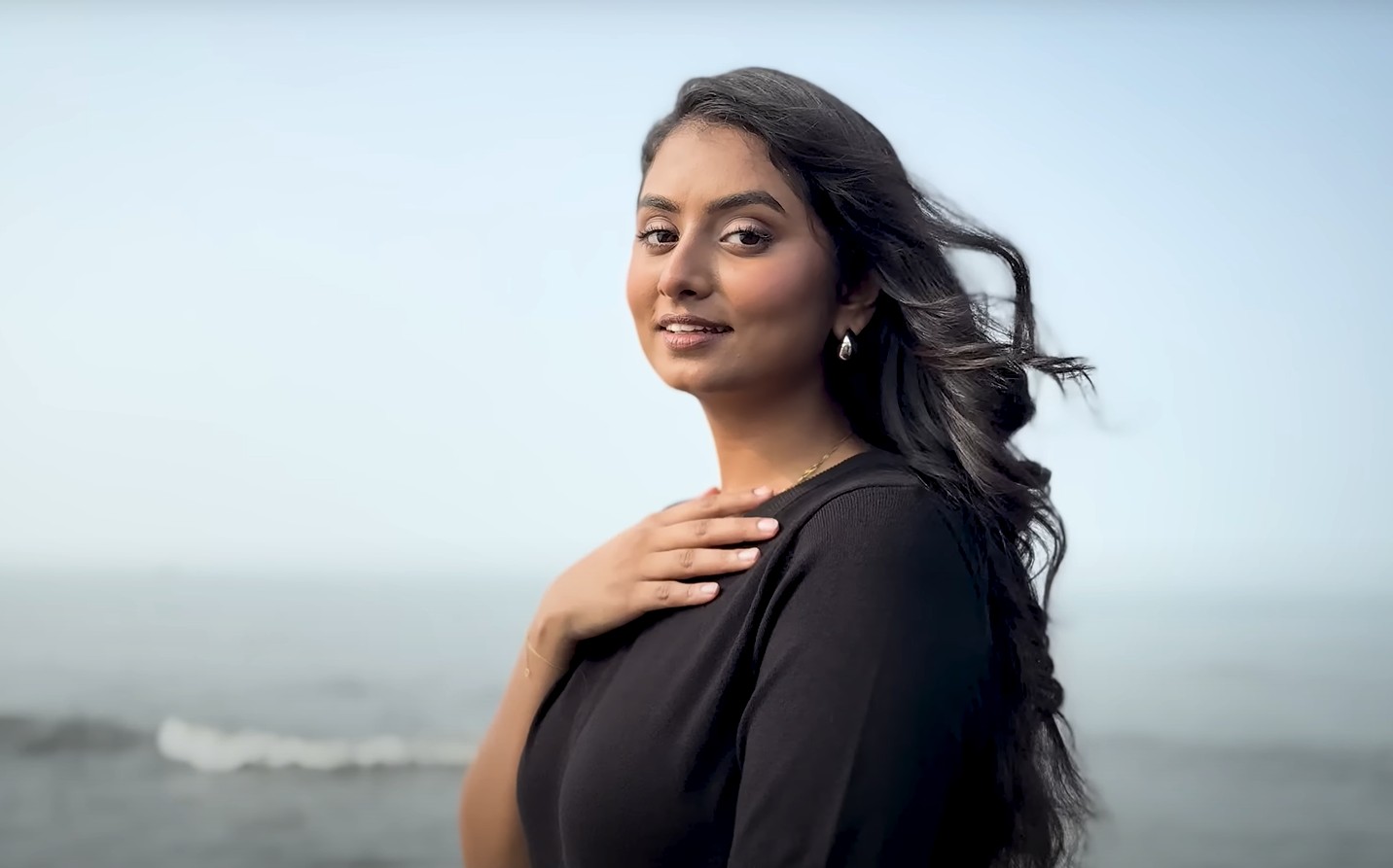 Vidhi Poddar in black dress looking into camera with sea in the background